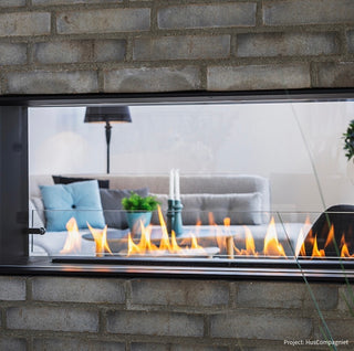 Modern fireplace with glass door showing flames, surrounded by a brick wall.