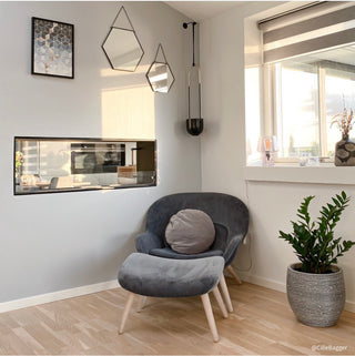 Modern interior with a gray armchair, plant, and wall art in a room with large windows.