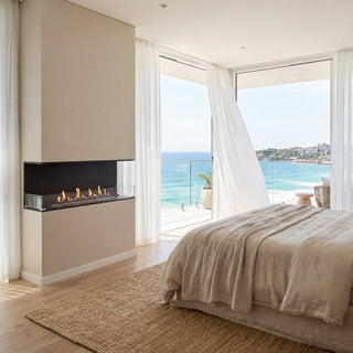 Modern bedroom with ocean view, bed, and fireplace.